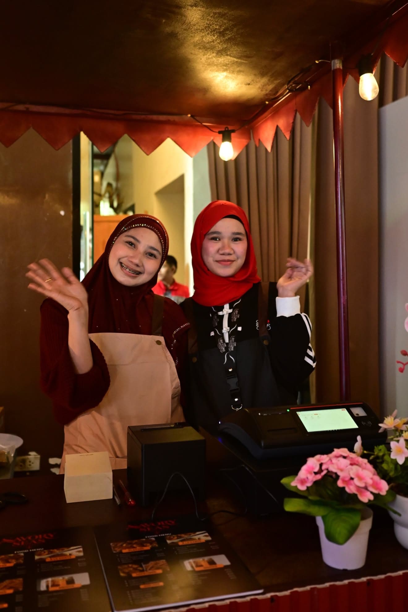 Two staff waving behind the counter with the UltraPOS terminal and receipt printer